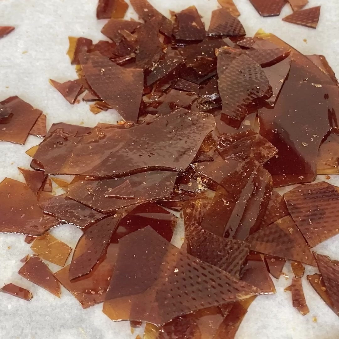 Thin amber caramel shards scattered across baking paper.